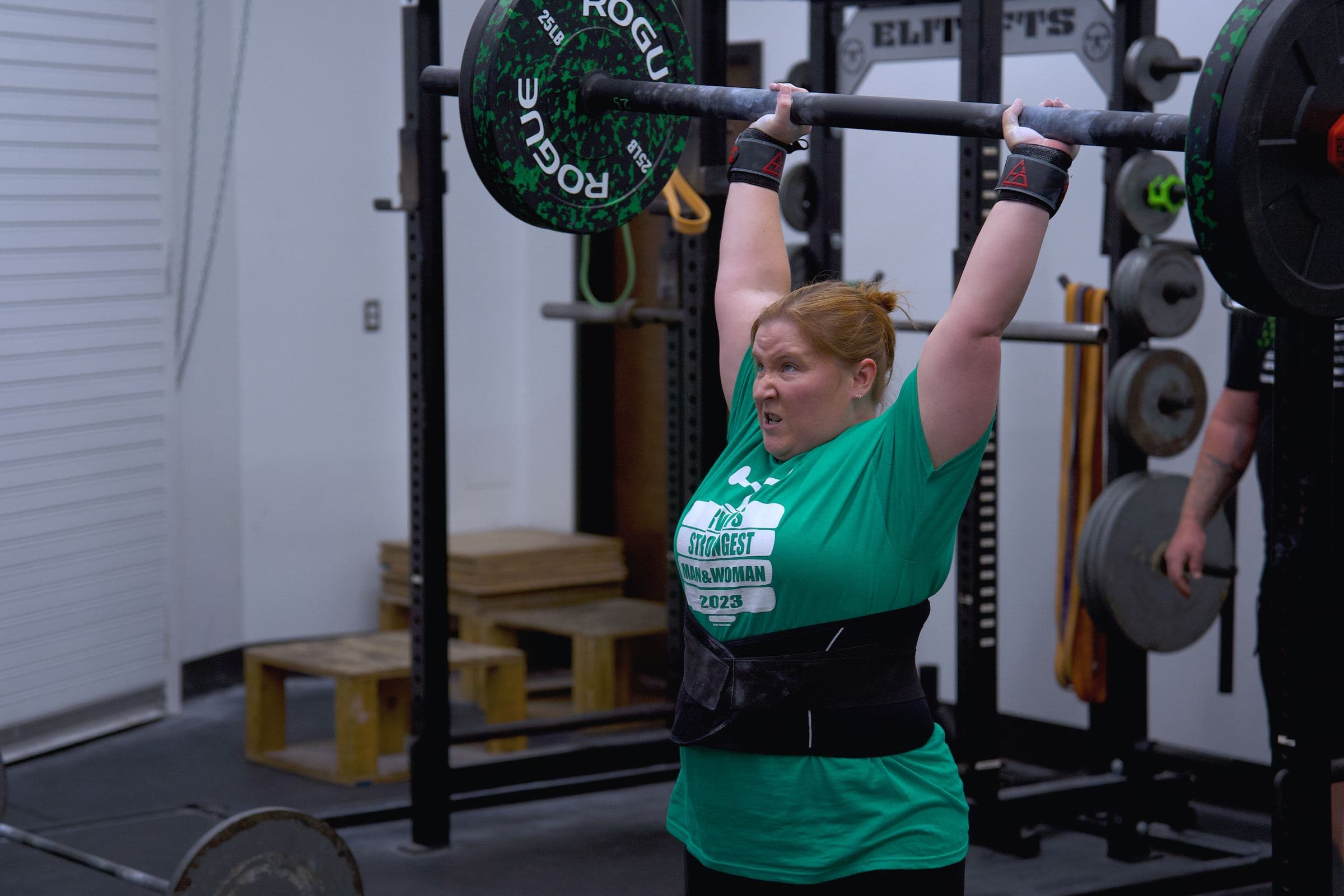An athlete pressing a barbell overhead in a training gym